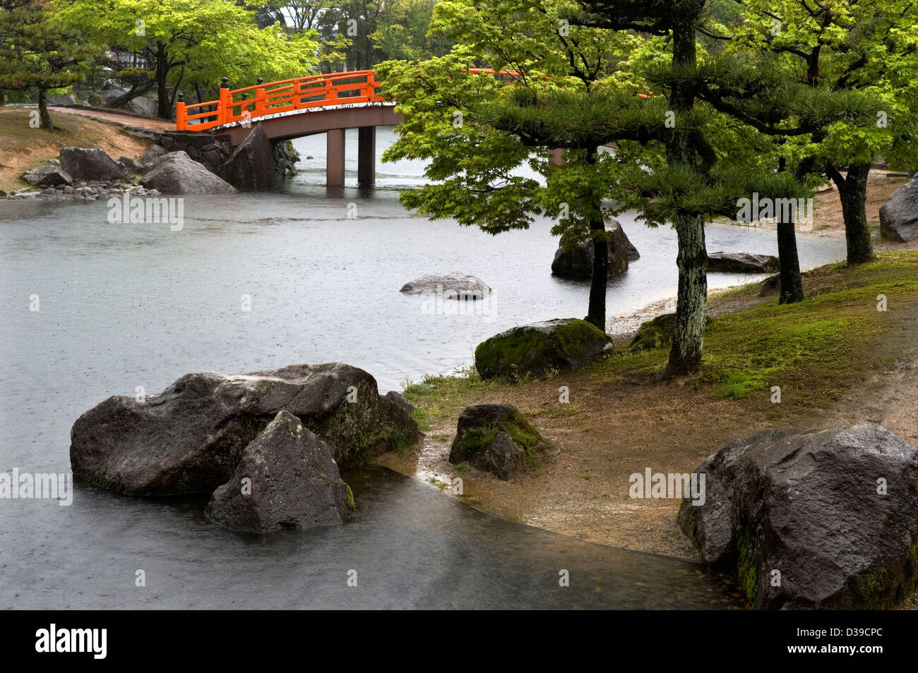 Shikibu Murashiki Koen park orange ponte ad arco oltre il giardino giapponese stagno in una piovosa, giornata di primavera. Foto Stock
