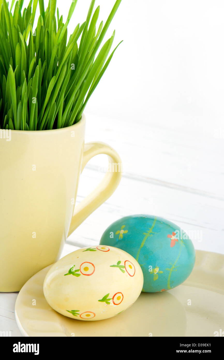 Due dipinti di uova di pasqua con una tazza di erba verde su bianco sullo sfondo di legno Foto Stock