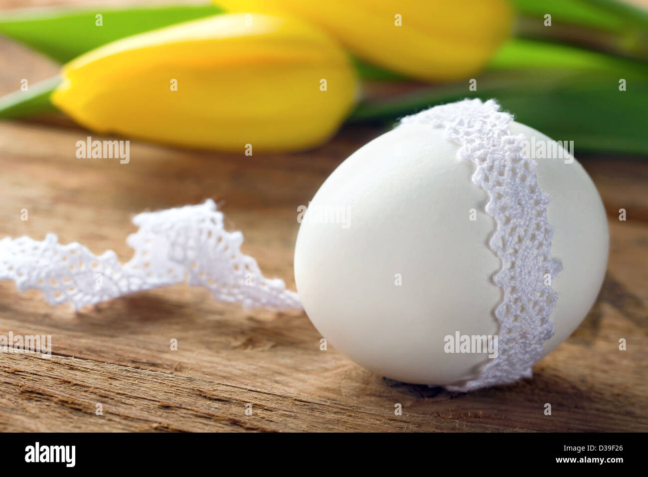 Bianco d'uovo di pasqua avvolto in pizzo, con tulipano giallo su legno sfondo rustico Foto Stock