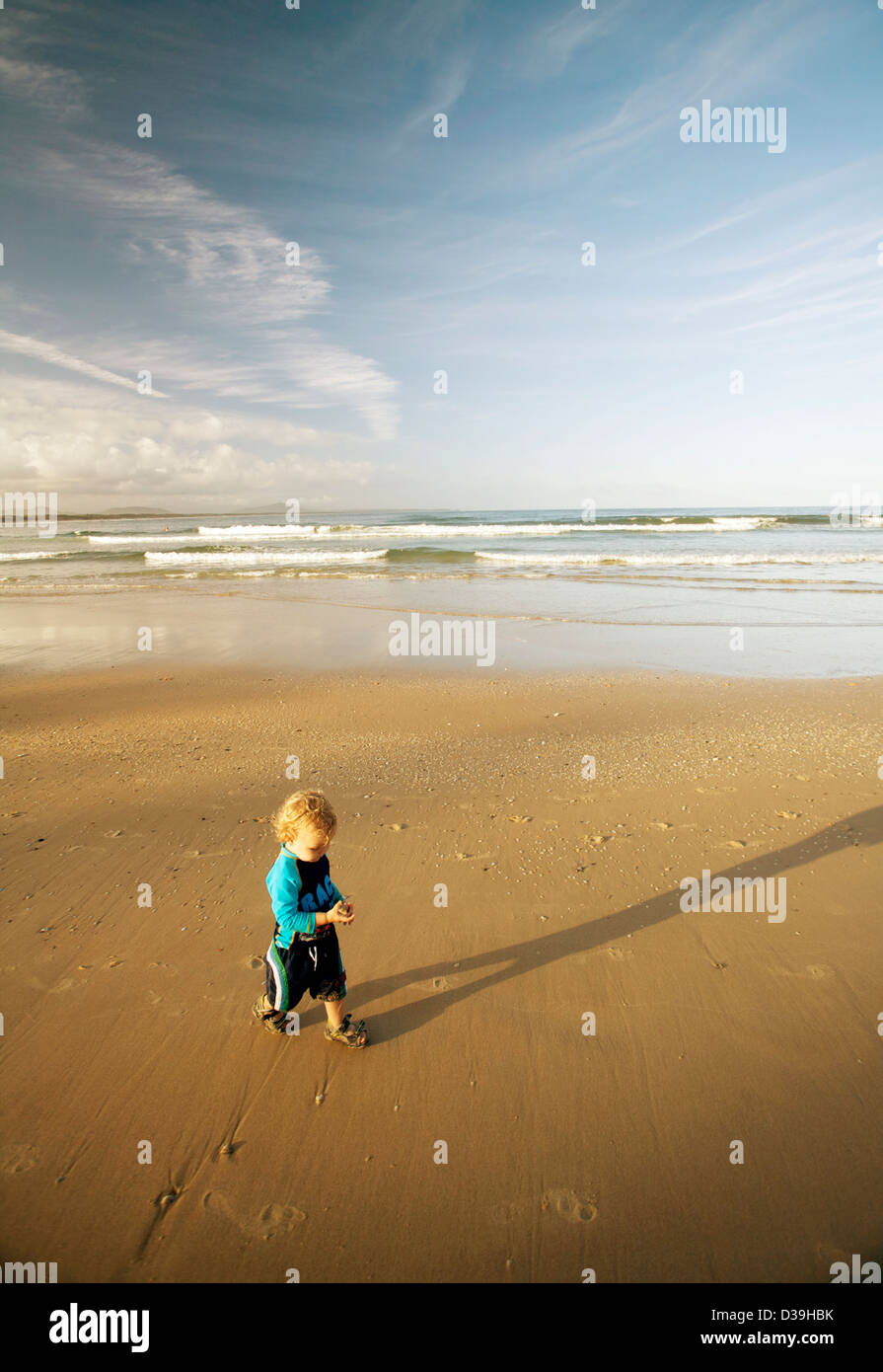 Piccolo ragazzo in costume da bagno blu / sunsuit su una spiaggia da sola Foto Stock