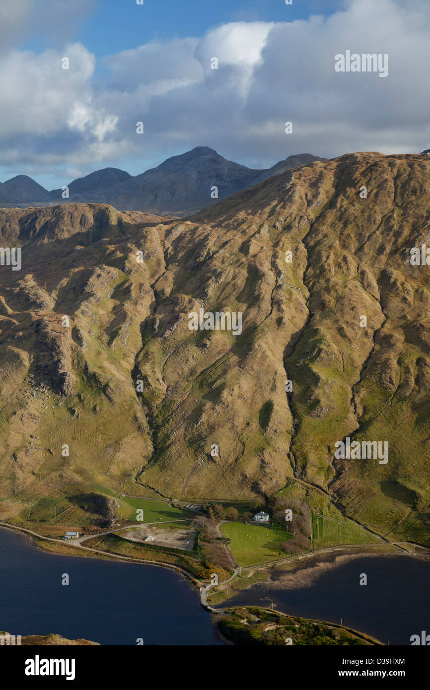 Agriturismo a distanza sulla riva di Kylemore Lough, sotto il Twelve Bens montagne. Connemara, nella contea di Galway, Irlanda. Foto Stock