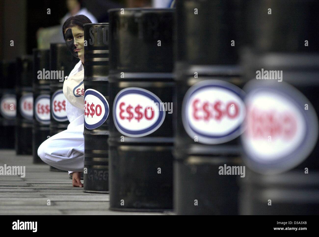 (Dpa) - Un attivista di Greenpeace si siede dietro i barili di olio con il logo e$$o della società Exxon Mobil durante una manifestazione di protesta a Amburgo, Germania, 29 maggio 2002. Foto Stock