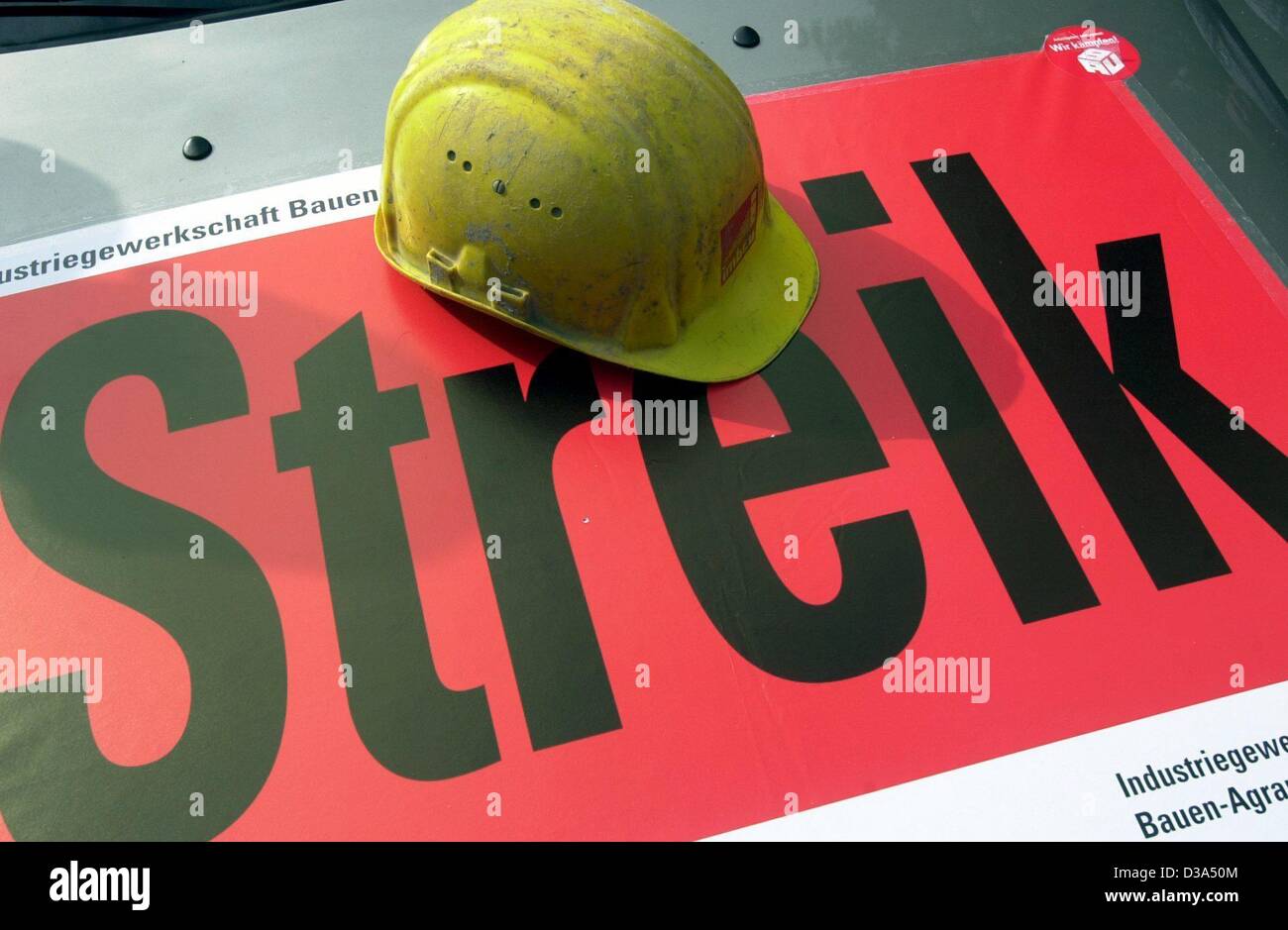 (Dpa) - Un lavoratore edile del casco giace su un poster che dichiara "treik' (strike), raffigurato su un sito di costruzione inHamburg, Germania, 17 giugno 2002. È il primo sciopero a livello nazionale nel settore della costruzione in Germania del dopoguerra. Il sindacato è stato in parla di un 4,5 per cento aumento dei salari wit Foto Stock