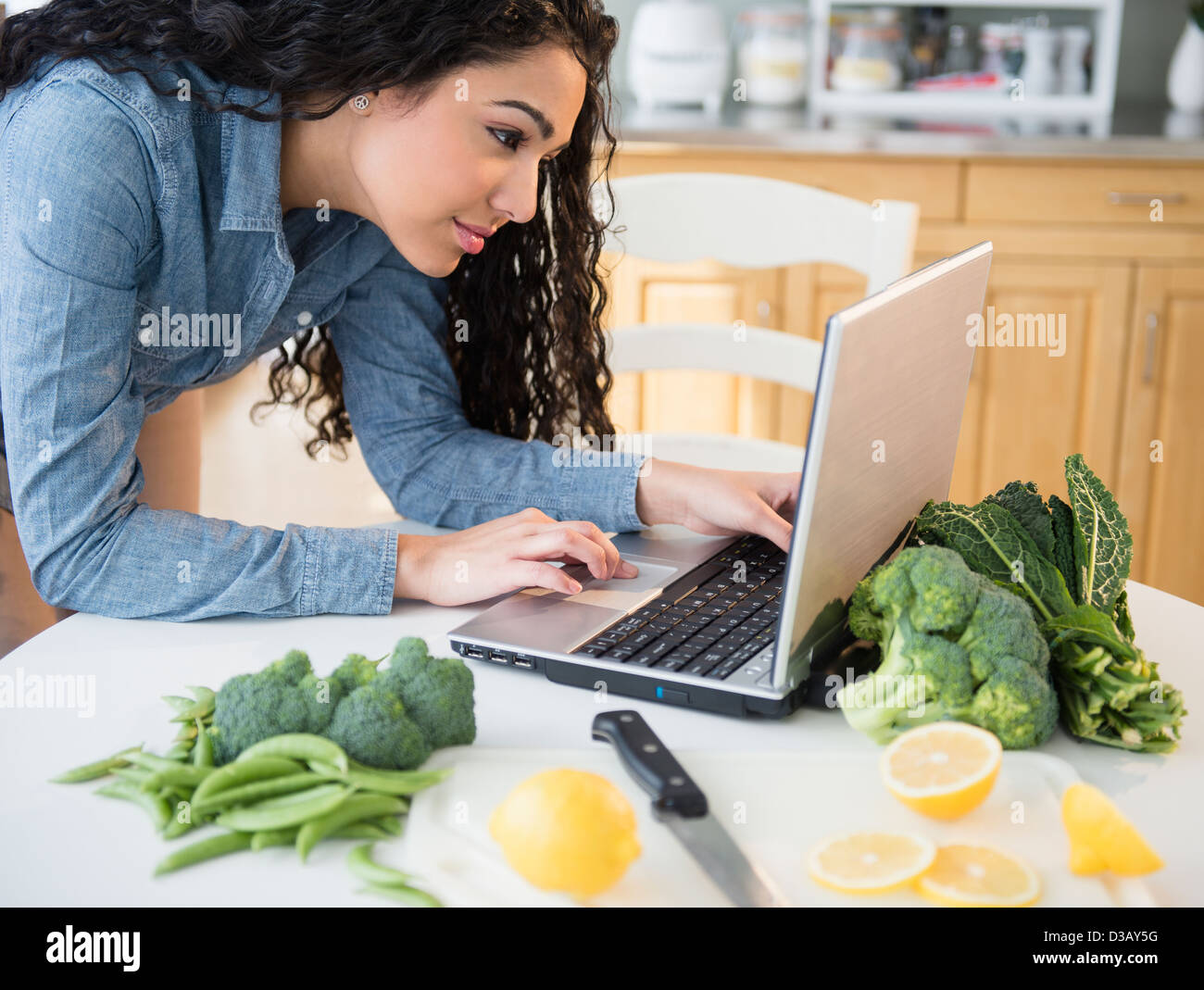 Donna ispanica utilizzando laptop per cucinare Foto Stock
