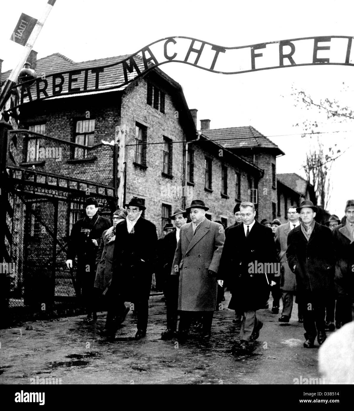 (Dpa file) - Un gruppo di Francoforte corte della giuria e numerosi giornalisti a piedi attraverso l'ex campo di concentramento cancello di Auschwitz (Oswiecim), Polonia, 14 dicembre 1964. L'iscrizione sul cancello di ferro si legge: "Arbeit macht frei" (lavoro vi rende liberi). È stata la prima visita della giuria su corte Foto Stock