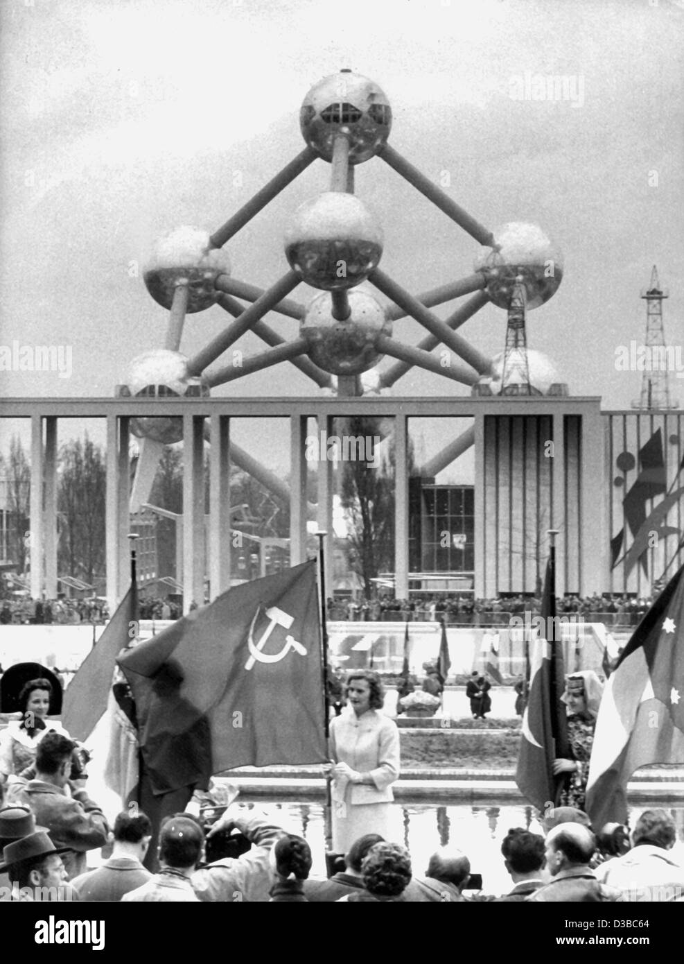 (Dpa file) - Una donna che porta una bandiera sovietica di fronte alla sala di ricevimento e la 'Atomium' speacially monumento costruito per la fiera mondiale di Bruxelles, 17 aprile 1958. È stata la prima fiera mondiale dopo la Seconda Guerra Mondiale. Foto Stock