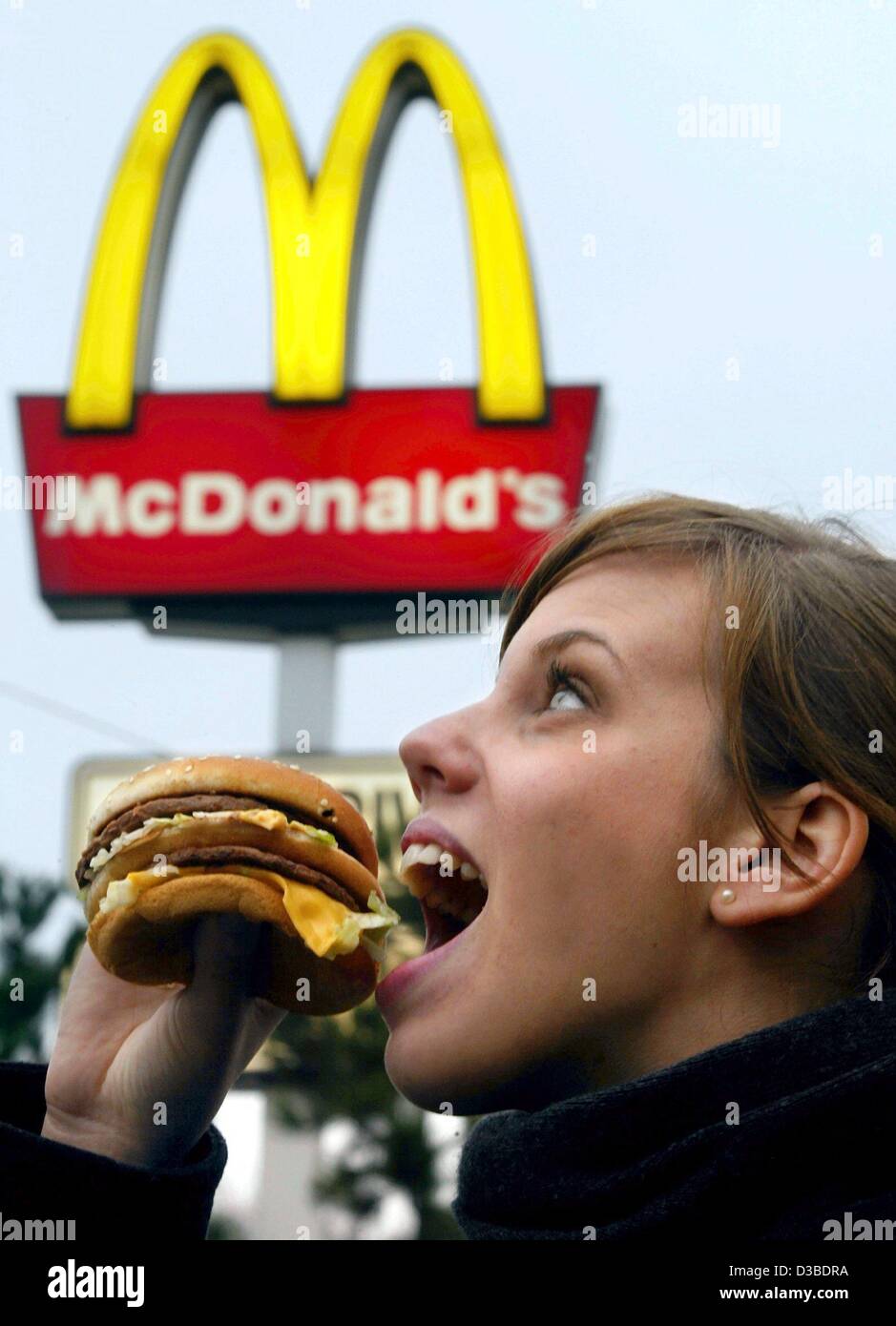 (Dpa) - Una giovane donna mangia un hamburger nella parte anteriore di un illuminato McDonald's logo in Duesseldorf, Germania, 23 gennaio 2003. Foto Stock