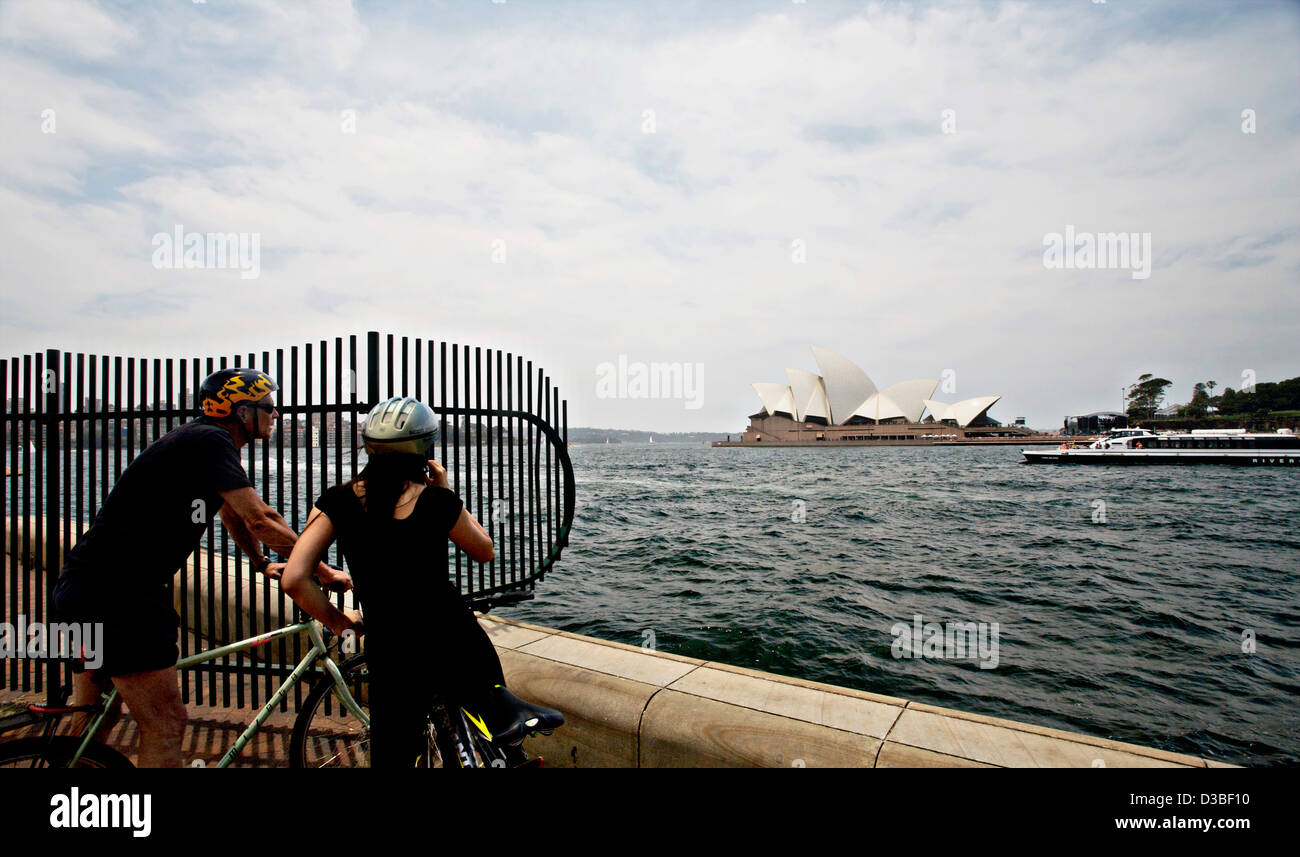 Un uomo e una donna su biciclette fermatevi e guardate la Opera House di Sydney, Australia Foto Stock