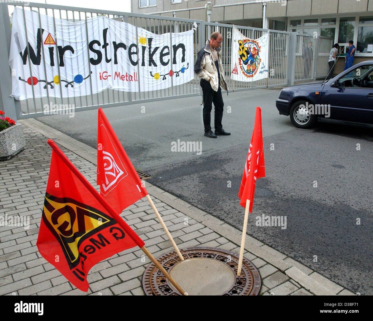 (Dpa) - bandiere dell'Unione tedesca IG Metall aderiscano al di fuori di un drenaggio e uno sciopero picket pende la sua testa come egli si trova di fronte a un banner "ci sono in sciopero" presso la porta chiusa di VW fabbrica di motori a Chemnitz, Germania orientale, 20 giugno 2003. In una mossa senza precedenti, la Germania del potente incontrato IG Foto Stock