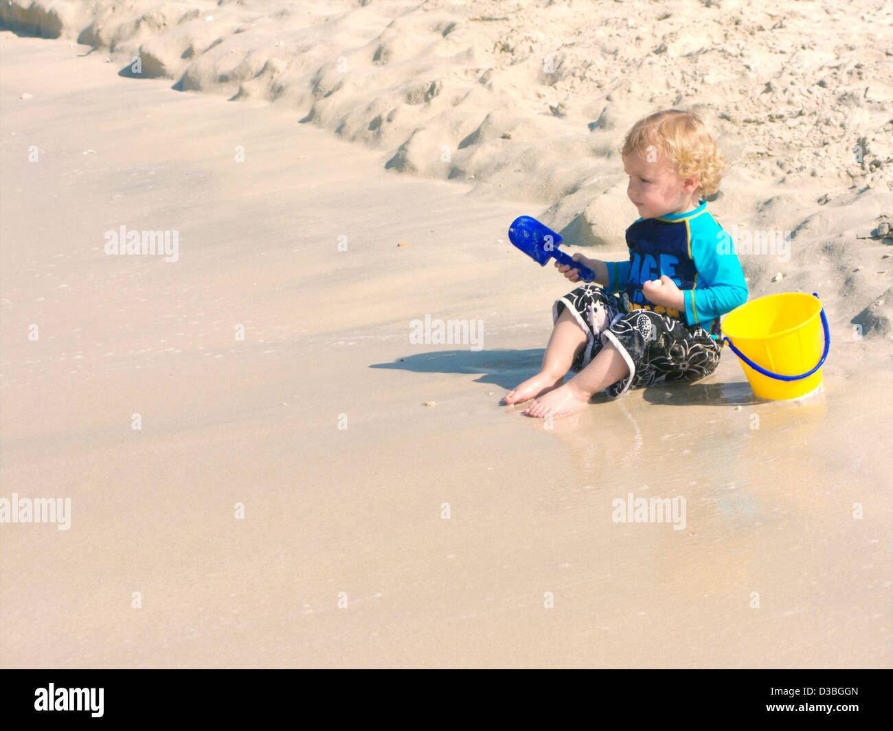 Piccolo ragazzo in costume gioca sulla spiaggia con un cucchiaio e capocorda Foto Stock