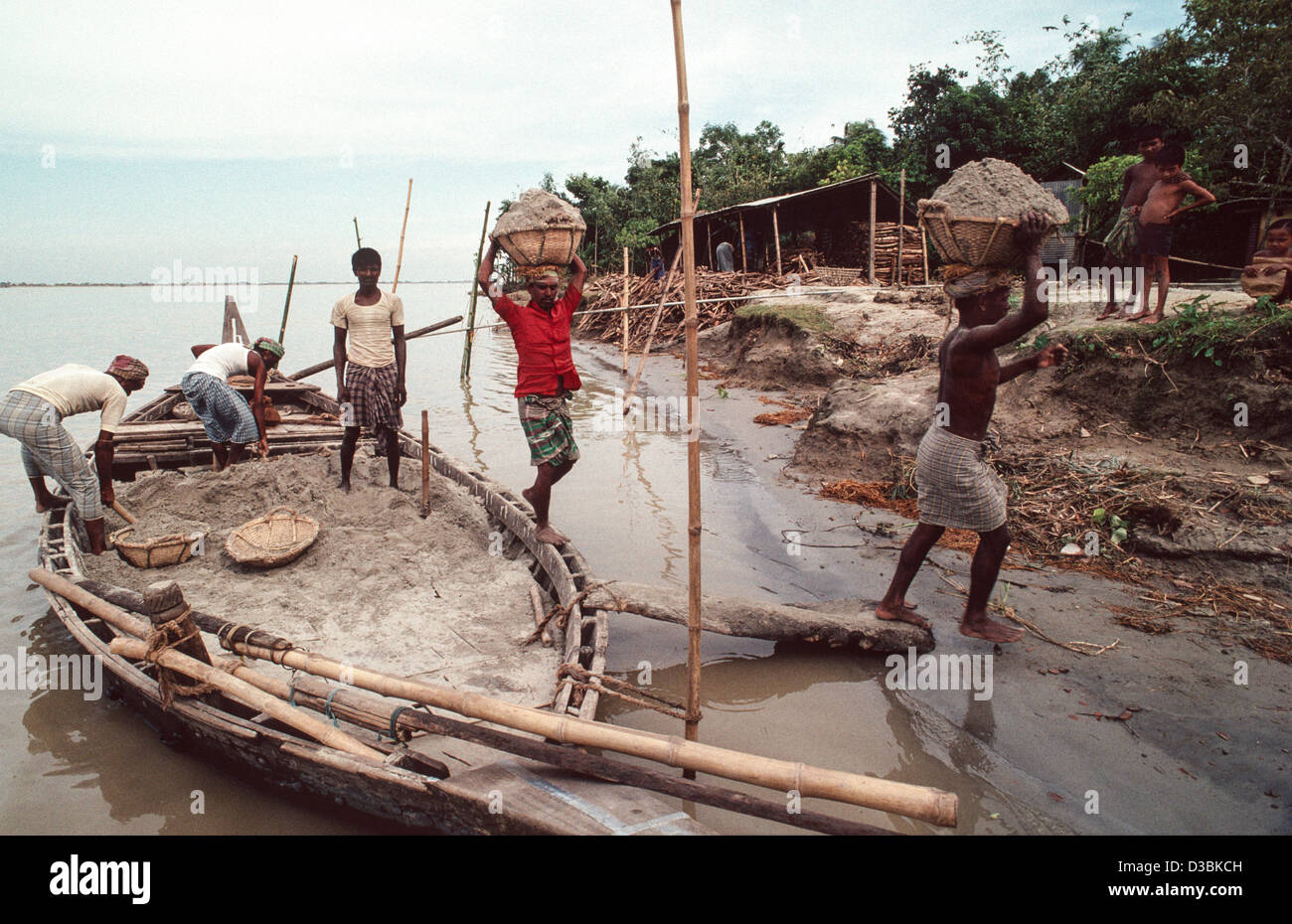 Facchini che trasportano i cestini di sabbia sulle loro teste prese da una barca locale per costruzione e la fabbricazione del cemento. Shiapur, Bangladesh Foto Stock
