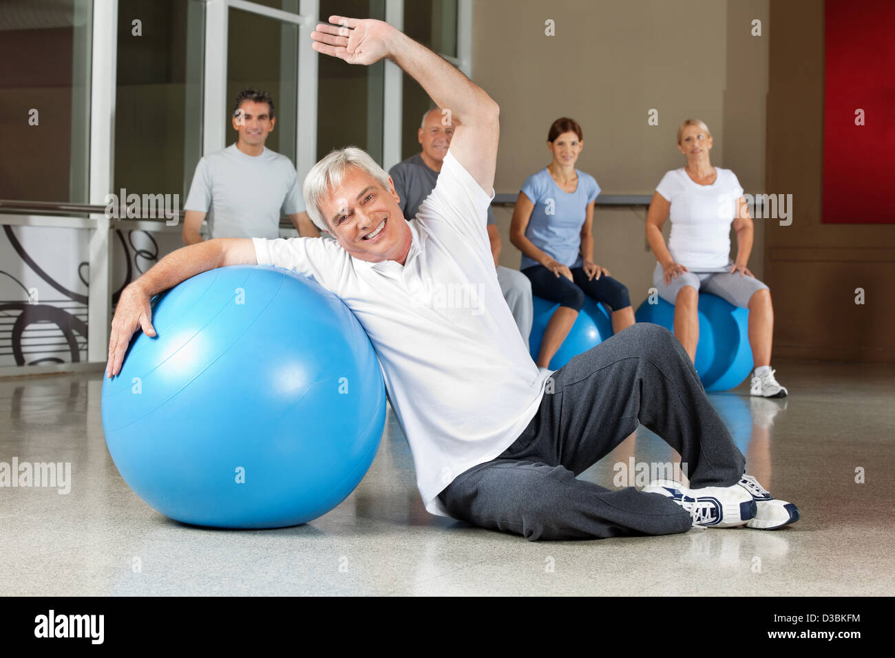 Uomo anziano facendo esercizi per la schiena con palla nel centro fitness Foto Stock