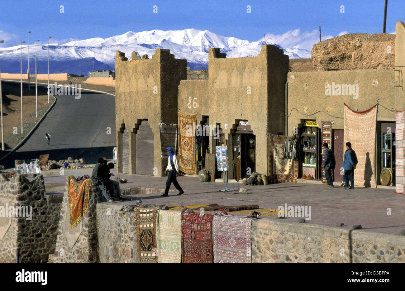 (Dpa) - i concessionari di tappeti di sedersi di fronte i loro negozi nella città di Ouarzazate, Marocco, 2001. Sullo sfondo le montagne Atlas può essere visto. Foto Stock