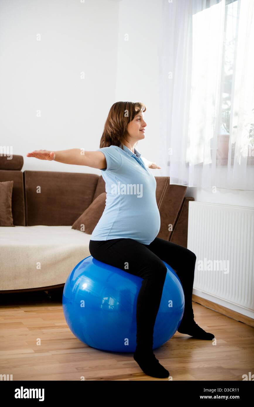 Donna incinta esercitando con montare la sfera a casa Foto Stock