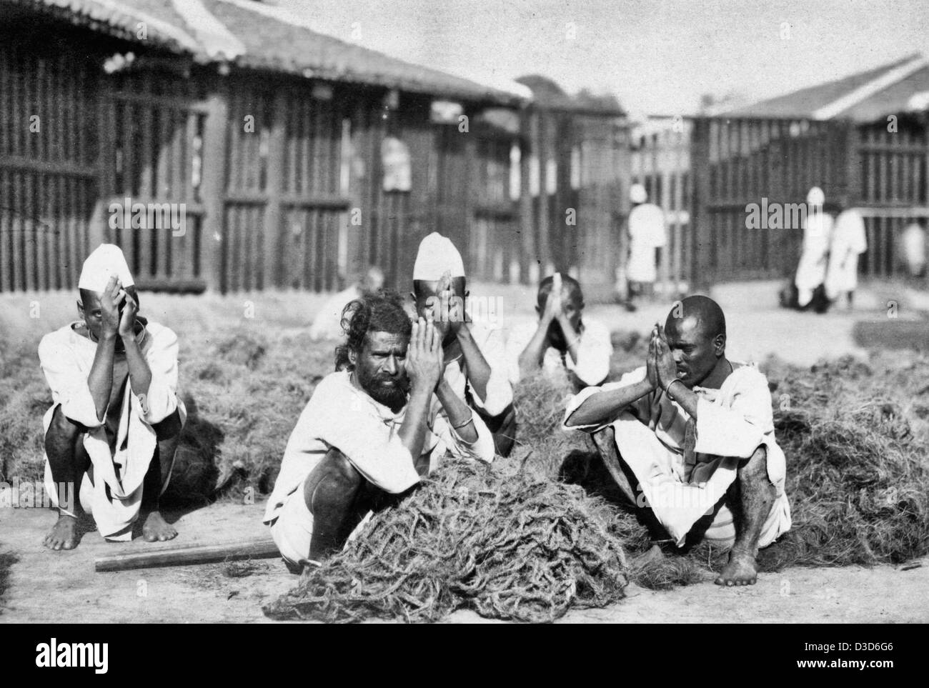 Cinque detenuti maschi squatting con mani premuti insieme nel mezzo di un materiale fibroso a Rangoon, Birmania, circa 1915 Foto Stock