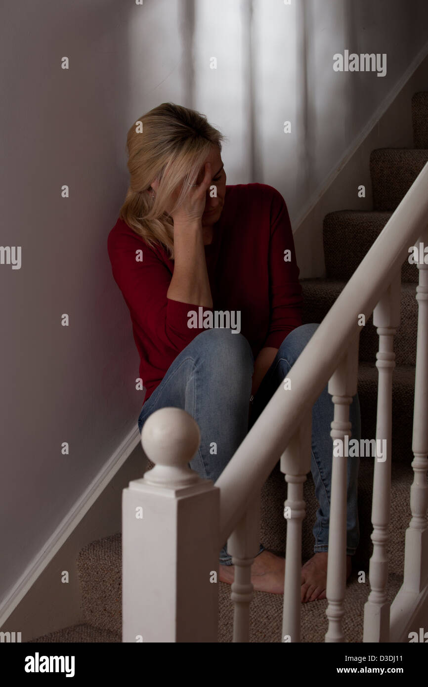 Donna bionda seduta nel buio da soli sui gradini, a casa, mano sul lato del suo viso è premuto. Foto Stock