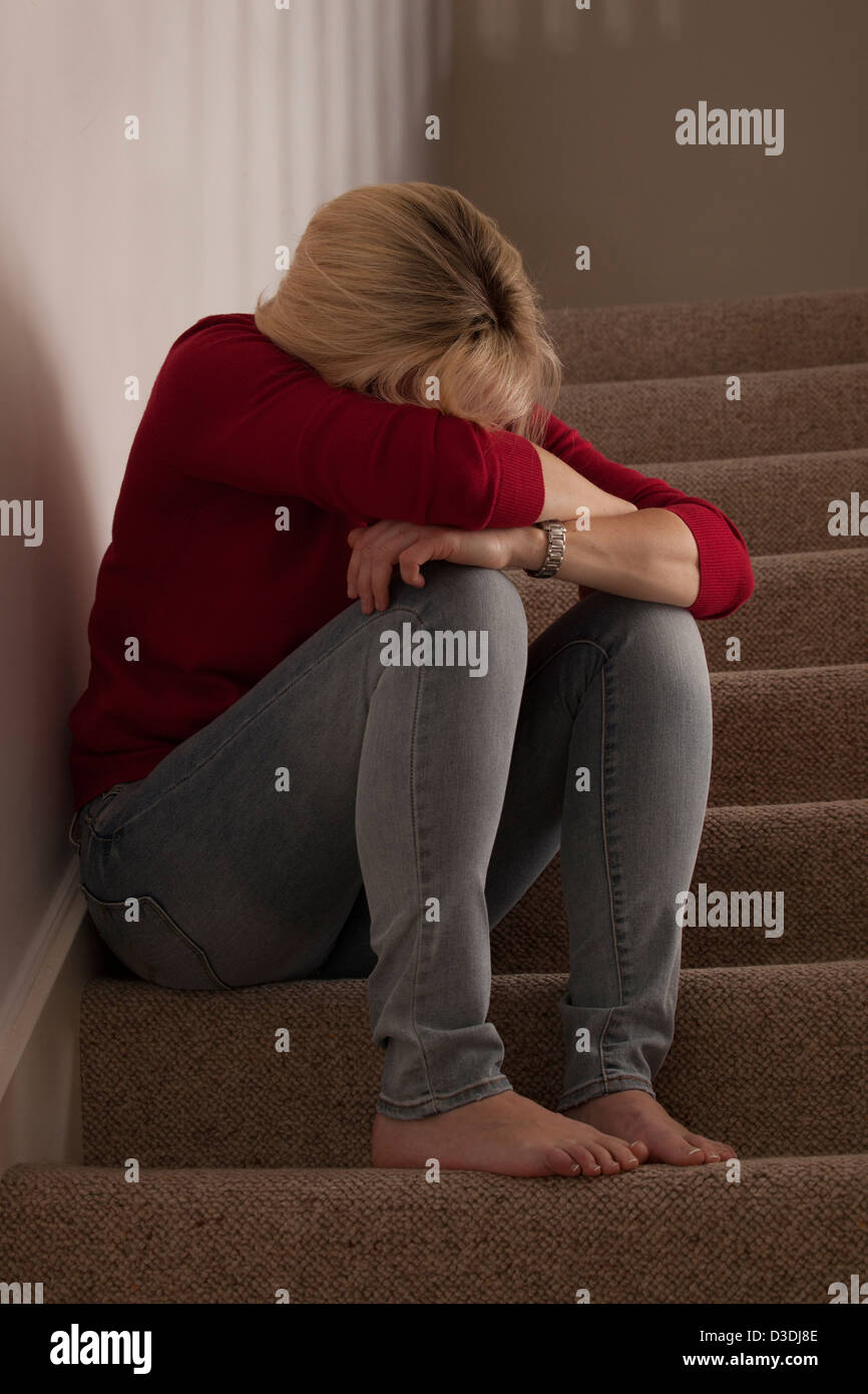 Donna bionda seduta da soli sui gradini, la testa piegata in avanti turbare o piangere. Foto Stock