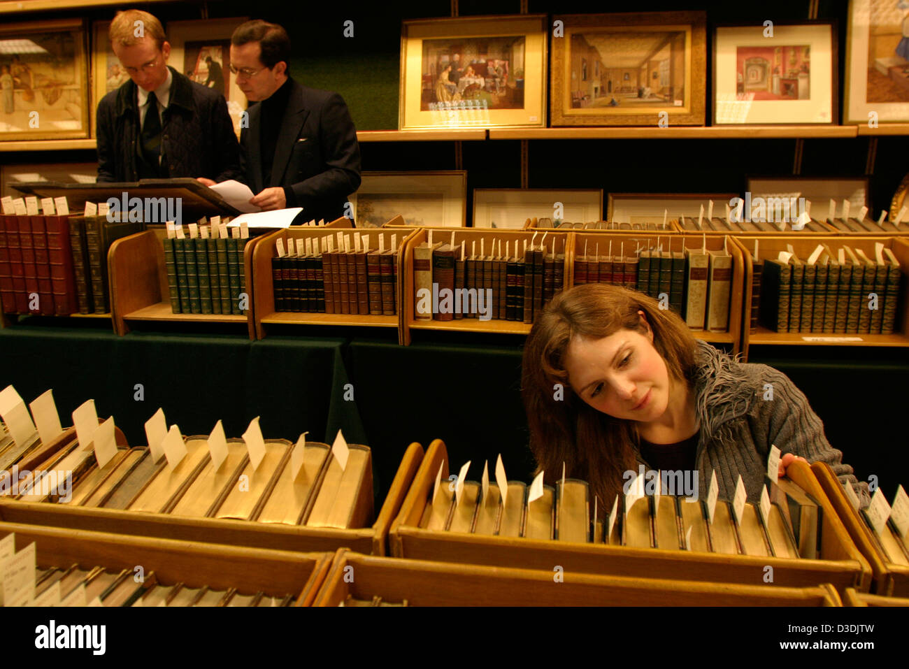 Una giovane donna guarda a libri a casa d'aste Christie's, South Kensington, mentre due uomini esaminare le stampe. Foto Stock