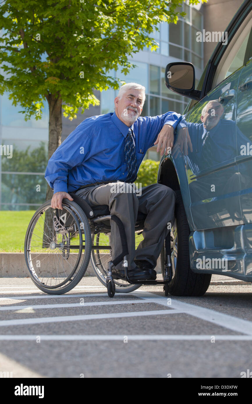 Uomo con la distrofia muscolare e il diabete in una sedia a rotelle a fianco di un furgone accessibile Foto Stock