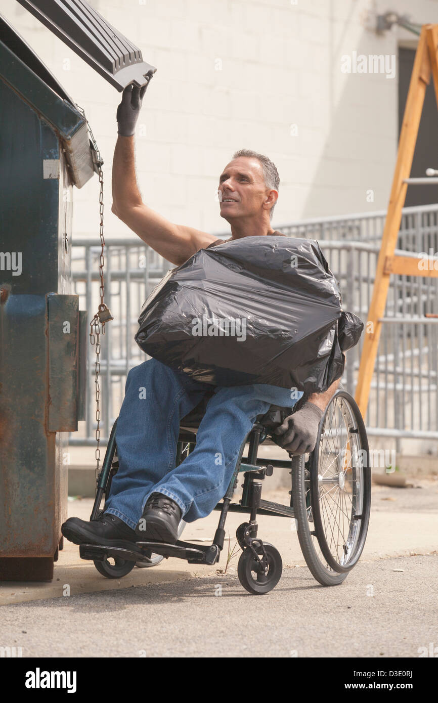 Banchina di carico lavoratore con lesioni al midollo spinale in una sedia a rotelle per mettere un sacco in un cassonetto Foto Stock