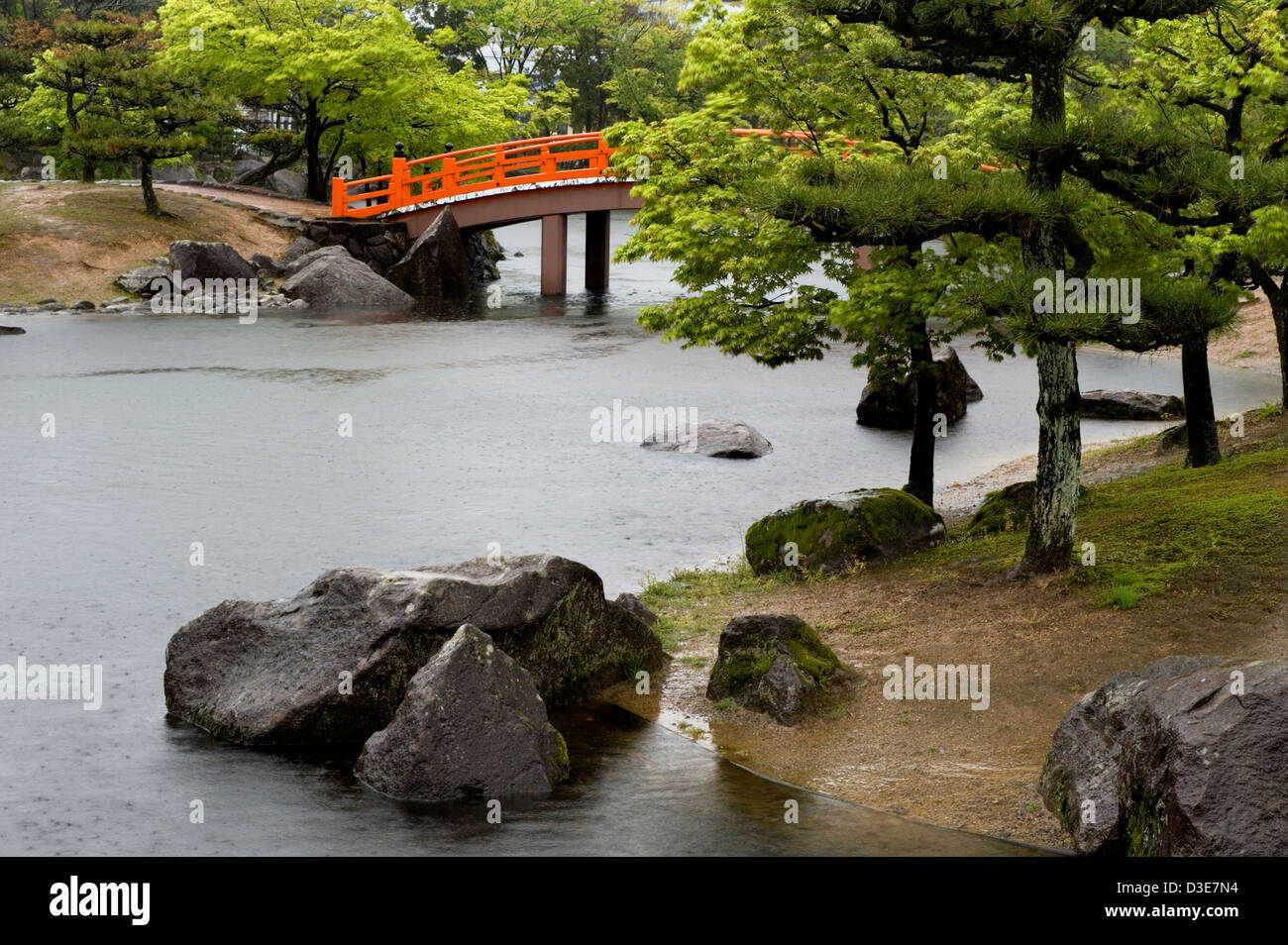 Shikibu Murashiki Koen park orange ponte ad arco oltre il paesaggio giapponese del laghetto in giardino in una piovosa, giornata di primavera. Foto Stock