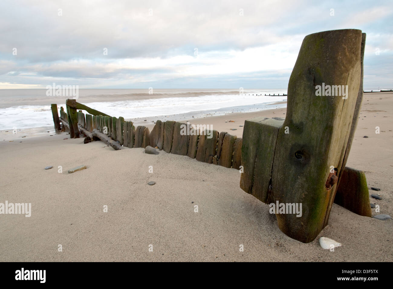 Indossati i frangiflutti in legno su una deserta spiaggia invernale Foto Stock