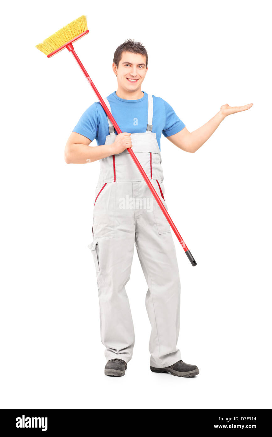 A piena lunghezza Ritratto di un detergente in modo uniforme con una scopa puntando con il suo braccio isolato su sfondo bianco Foto Stock