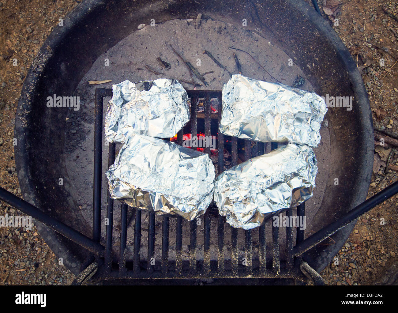Cibi avvolti in un foglio di alluminio è la cottura in un campeggio in una buca per il fuoco Foto Stock