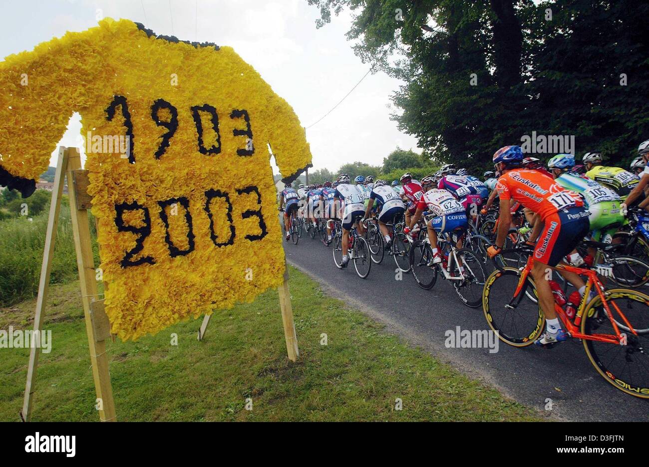 (Dpa) - i ciclisti passano da un grande 'maillot jaune" (maglia gialla) realizzata con fiori di carta segna il centenario del Tour de France durante la seconda tappa del Tour de France da La Ferte-sous-Jouarre a Sedan, Francia, 7 luglio 2003. Foto Stock