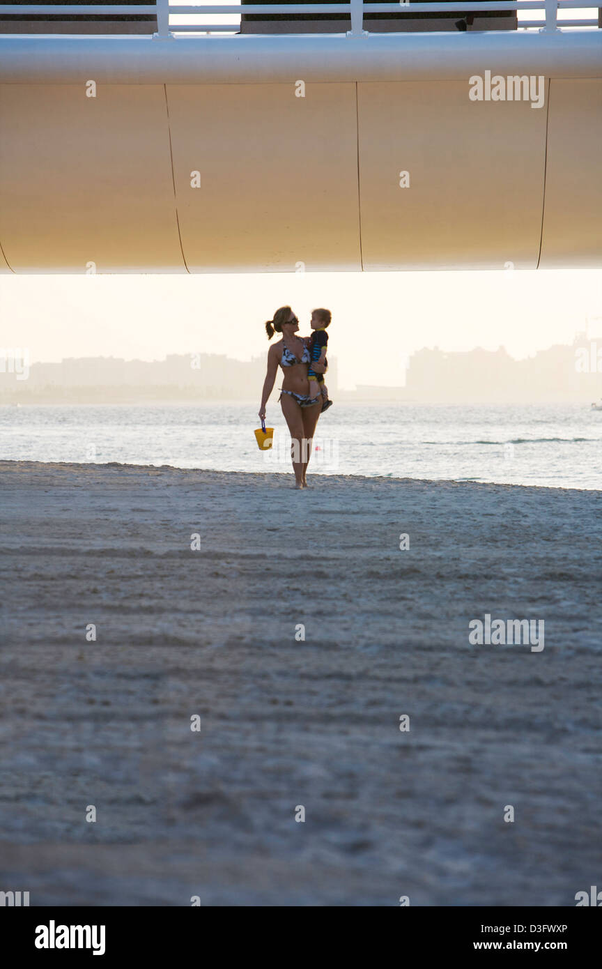 Donna e bambino a piedi lungo la spiaggia al di sotto della strada di accesso al Burj Al Arab sette stelle di Dubai Foto Stock