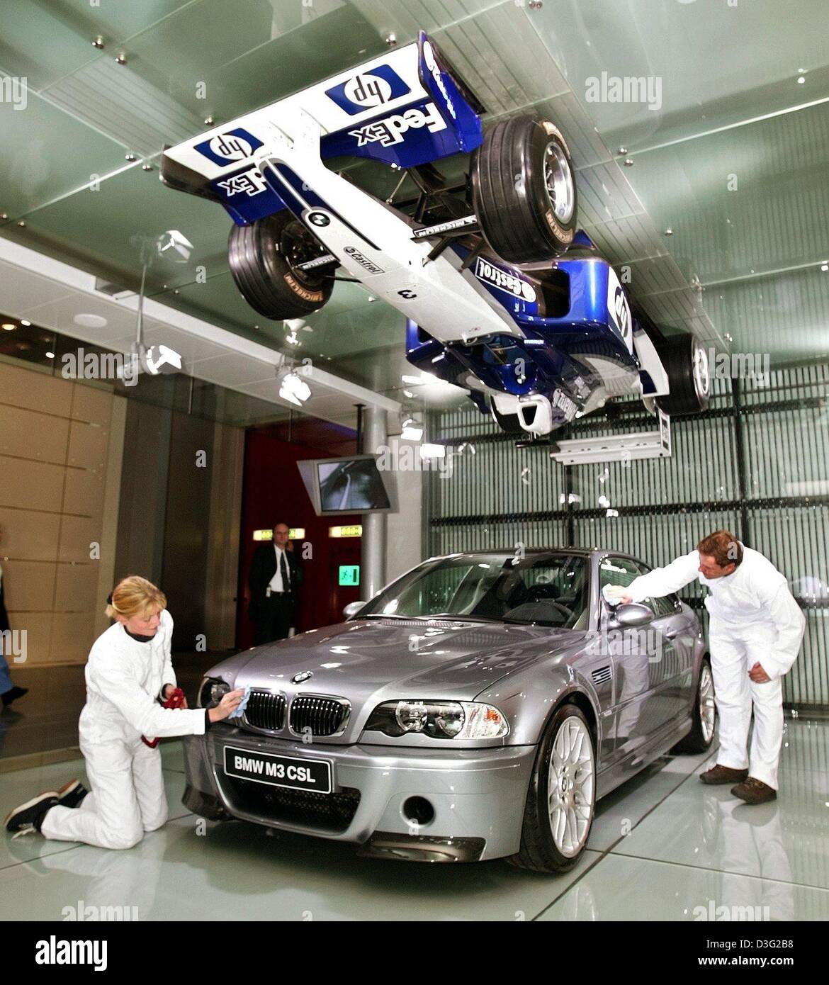 (Dpa) - I dipendenti della BMW auto costruttore di cera e polacco della BMW nuovo modello 'M3 CSL' e dal soffitto pende una formula one racing car con un motore BMW in esso a Ginevra l 'Automobilesalon', la vettura mostra e fiera, a Ginevra, Svizzera, 4 marzo 2003. Il 'Automobilesalon' è la prima evidenziare nella corrente europea anno di business per i costruttori e i progettisti. Foto Stock
