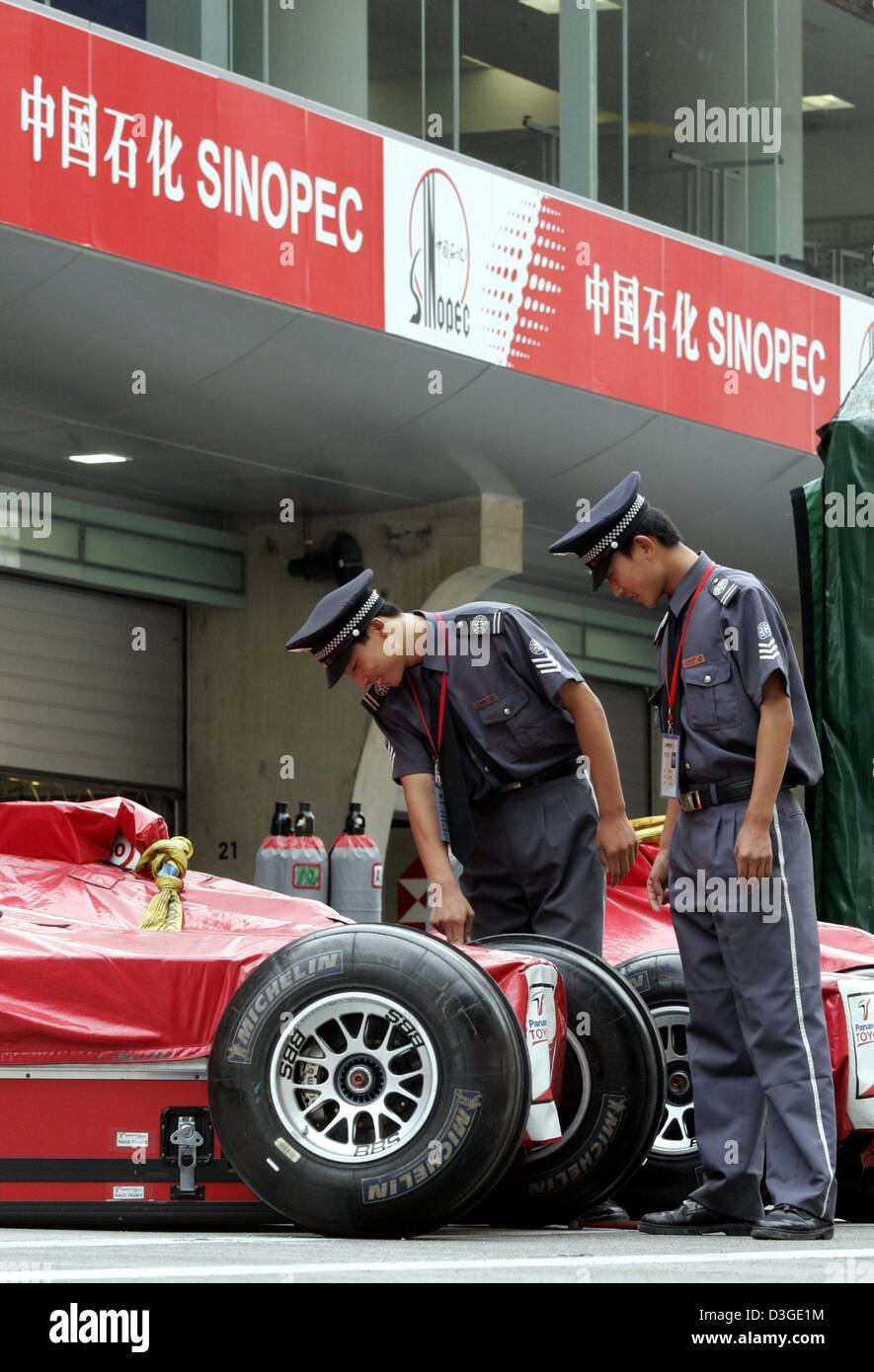 Cinese il personale di sicurezza curiosamente guardare un parcheggiato le corse di Formula Uno auto in pit lane della gara di Formula Uno corso in Cina a Shanghai, 21 settembre 2004. Il Gran Premio di Cina si terrà su la nuova costruzione della pista per la prima volta domenica 26 settembre. Foto Stock