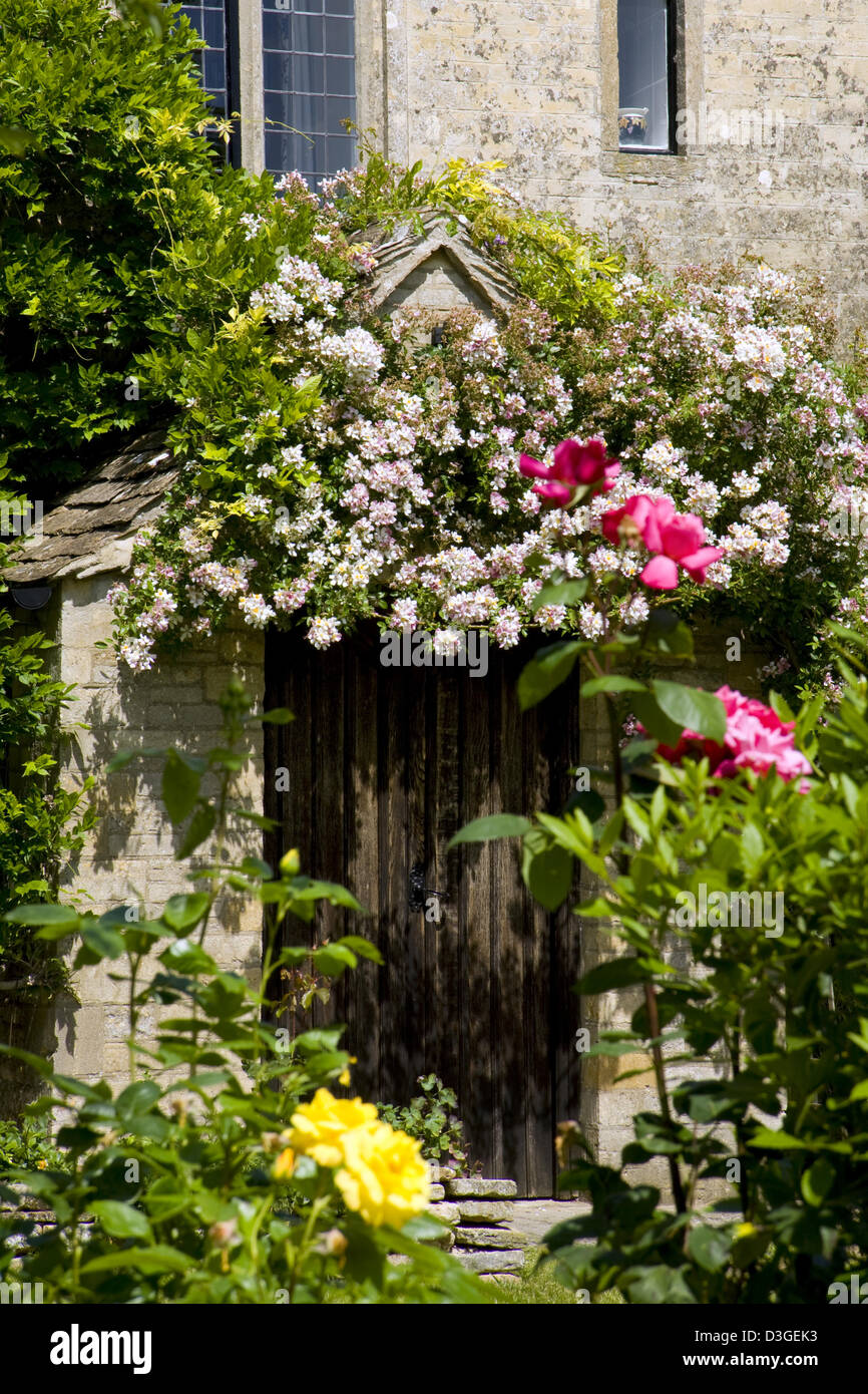 Un vecchio cottage in pietra con rose rampicanti oltre la porta Gloucestershire, England, Regno Unito Foto Stock