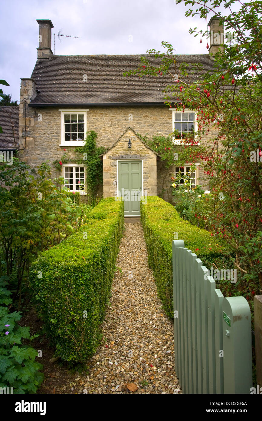 Un cancello aperto che conduce in basso lungo il giardino coperto il percorso di un idilliaco cottage porta anteriore, Gloucestershire, England, Regno Unito Foto Stock