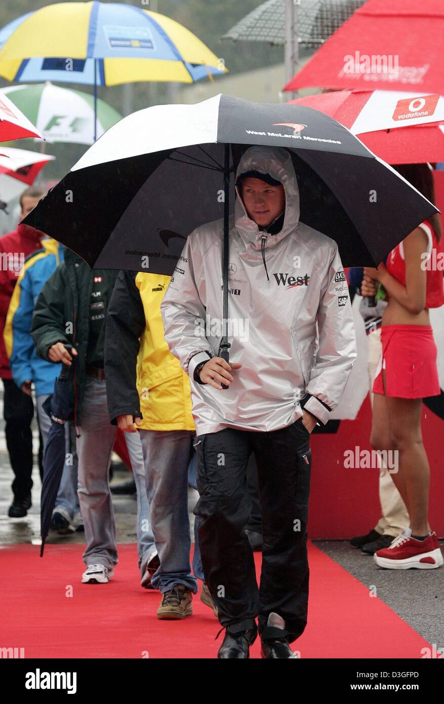 (Dpa) - Finlandese pilota di Formula 1 Kimi Raeikkoenen (team McLaren-Mercedes) passeggiate intorno con un ombrello durante il piovoso presentazione del driver prima del Gran Premio d'Italia a Monza, Italia, 12 settembre 2004. Foto Stock