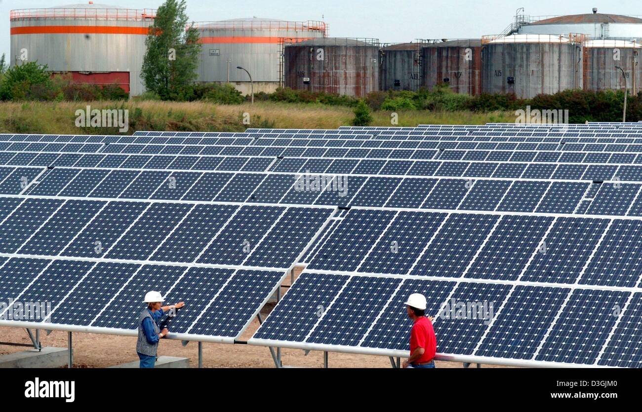 (Dpa) - due dipendenti a stare di fronte di righe di grandi pannelli solari a uno dei più grandi in tutto il mondo impianti fotovoltaici in Krumpa, Germania, 30 giugno 2004. La centrale solare è stato costruito nei locali di un ex raffineria di petrolio e copre un aera di circa 160.000 metri quadrati con un massimo di 25, 000 mono e poli cristallino di moduli solari in appoggio su 777 telai metallici. La potenza pl Foto Stock