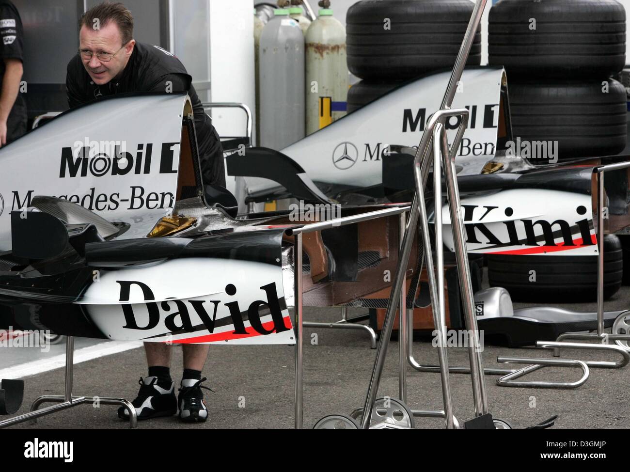 (Dpa) - Un McLaren-Mercedes meccanico sorge accanto alle vetture da corsa di Formula Uno driver Kimi Raeikkoenen e David Coulthard sulla gara di Magny Cours corso in Francia, giovedì 1 luglio 2004. Il Gran Premio di Francia sarà in corso domenica 4 luglio 2004. Foto Stock
