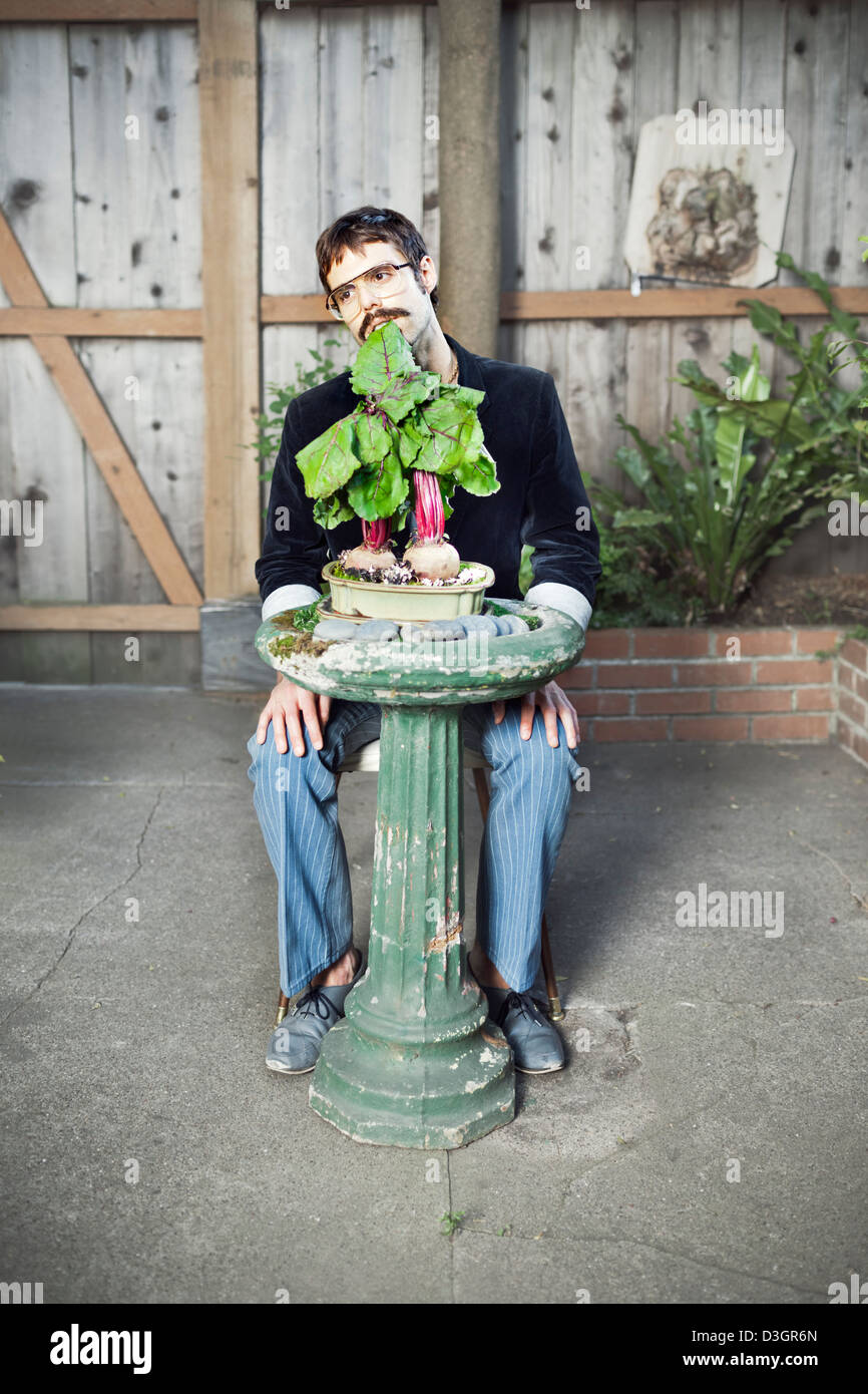 Hipsters e beatnik - una giovane hipster uomo con i baffi e bicchieri di mangiare ancora piantate bietole su un bagno uccelli nel suo giardino Foto Stock