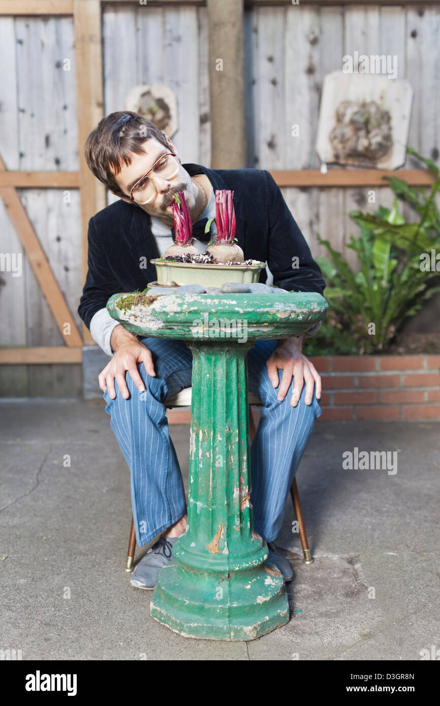 Hipsters e beatnik - una giovane hipster uomo con i baffi e bicchieri di mangiare ancora piantate bietole su un bagno uccelli nel suo giardino Foto Stock