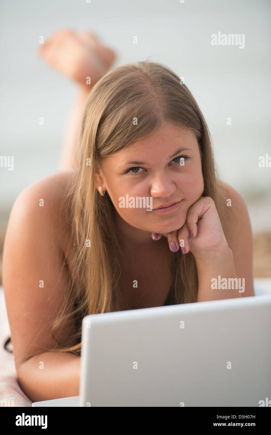Studentessa sdraiato sulla spiaggia e funziona con computer portatile bianco Foto Stock