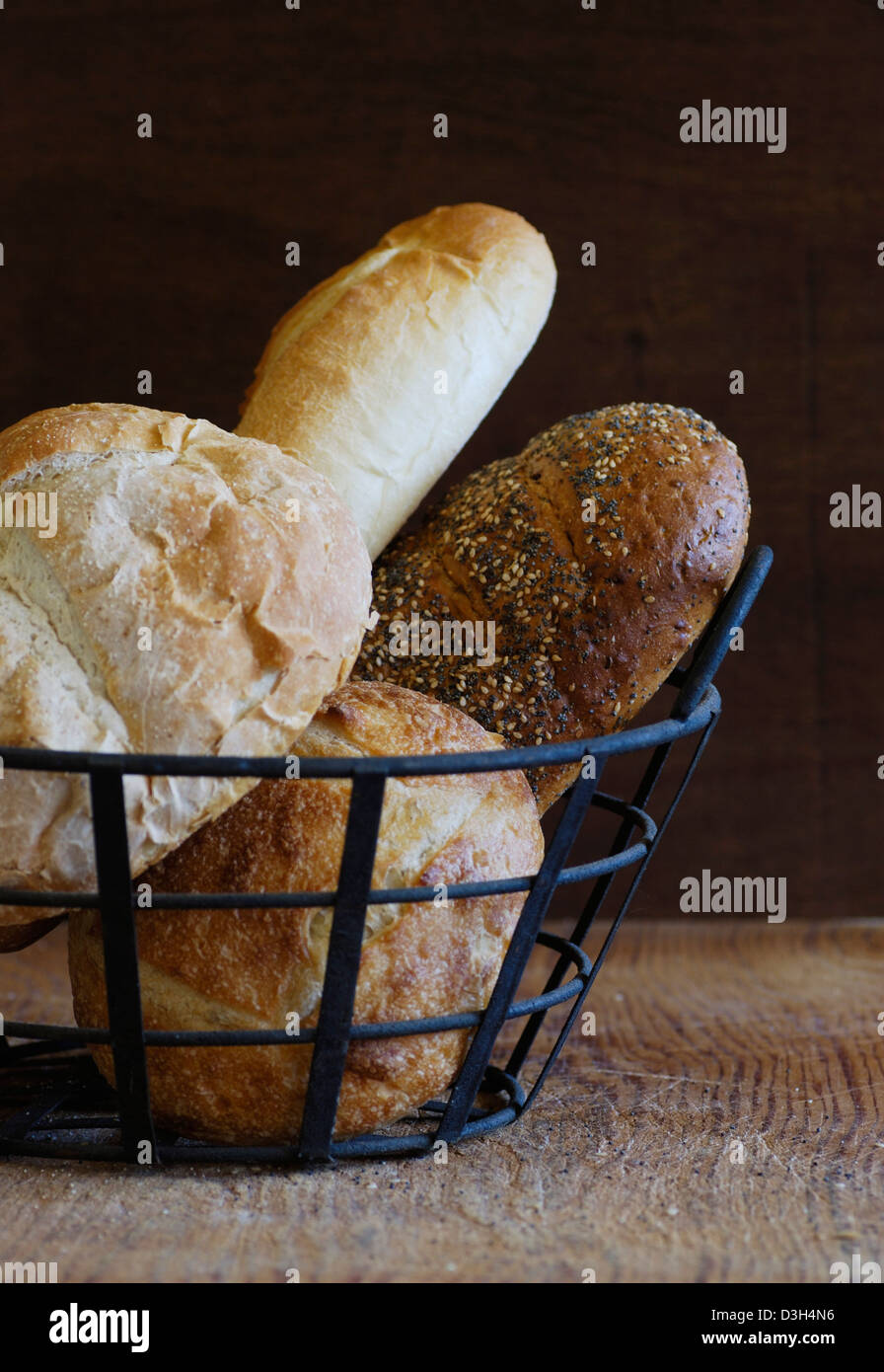 Il pane artigianale pani in filo metallico cesto su legno tagliere, Sourdough, Francese, semi di papavero, semi di sesamo, Mini filone di pasta acida Foto Stock