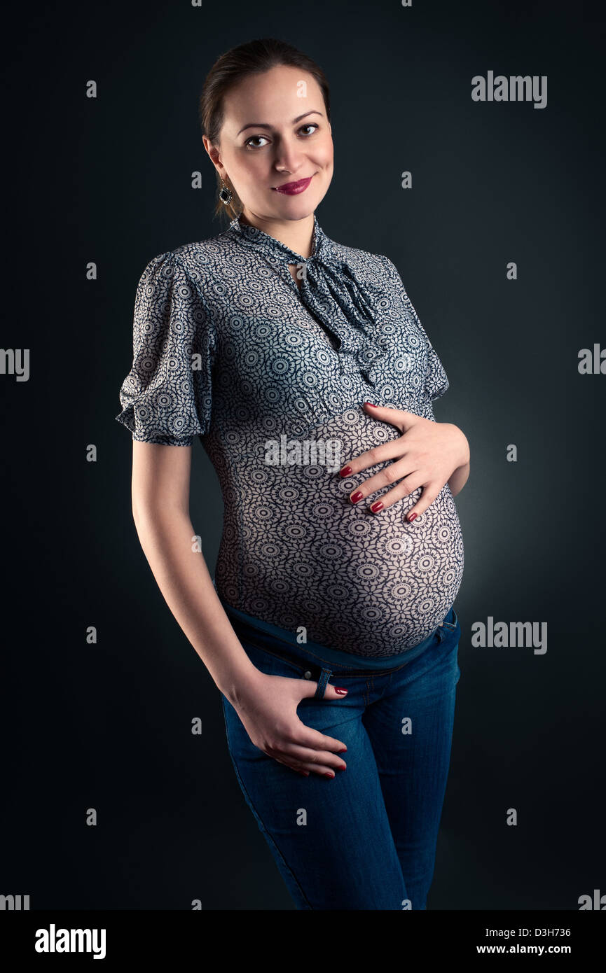 Studio shot della donna incinta in camicetta e jeans Foto Stock