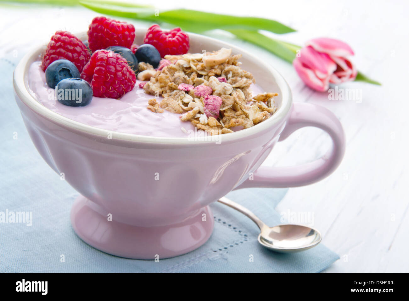 Frutti di bosco e yogurt in rosa elegante tazza con cereali granola, rosa tulip in background Foto Stock