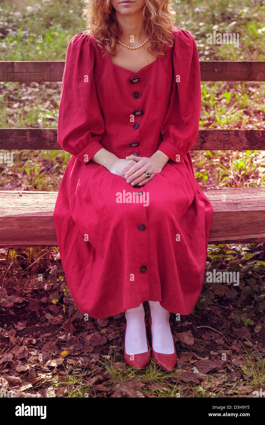 Una donna in rosso, abito rustico su una panca in legno Foto Stock