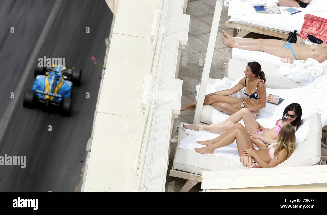 (Dpa) - italiano in Formula Uno pilota Giancarlo Fisichella di Renault (L) comanda la sua vettura da gara mentre le donne non identificato in bikini prendere il sole sul divano letti durante il Grand Prix di Monaco sessione di addestramento a Monte Carlo, Monaco, sabato 21 maggio 2005. Foto Stock