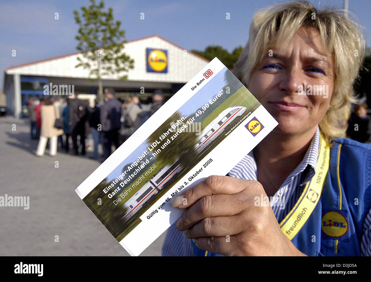 (Dpa) - assistente vendite Ramona Wienholz presenta un biglietto del treno come lei a stare di fronte ad un ramo del tedesco rivenditori discount Lidl ad Augsburg, in Germania, giovedì, 19 maggio 2005. Un gruppo di coda dei clienti al di fuori dell'entrata. Lidl negozi sono ora vendono i biglietti del treno per la prima volta. In alcune delle società delle filiali i biglietti sono andati esauriti in pochi minuti. Foto Stock