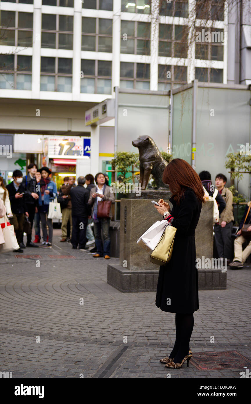 Una giovane donna in attesa di fronte alla statua di Hachiko a Shibuya mentre texting, Tokyo, Giappone Foto Stock