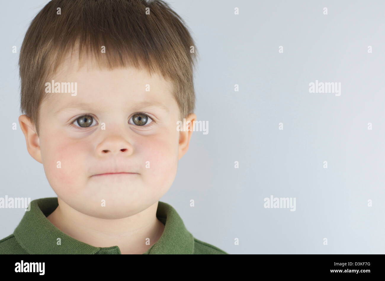 Grave e determinato 2 anno vecchio ragazzo guardando dritto in telecamera, labbra pursed con occhi verdi ampia e chiara, copia dello spazio. Foto Stock