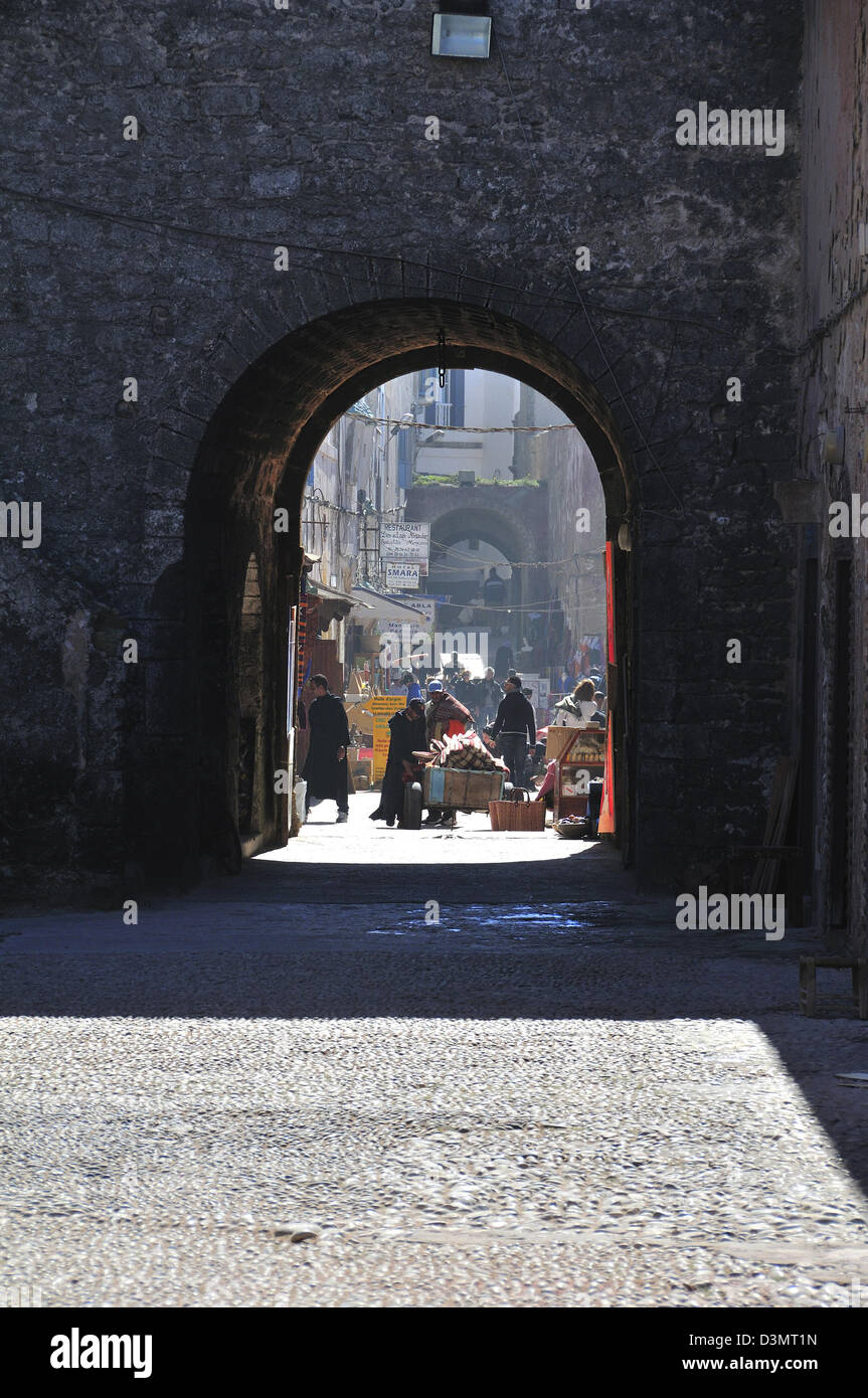 Vista attraverso il vecchio arco verso i piccoli negozi e i lavoratori la medievale città murata di Essaouira sulla costa atlantica del Marocco Foto Stock