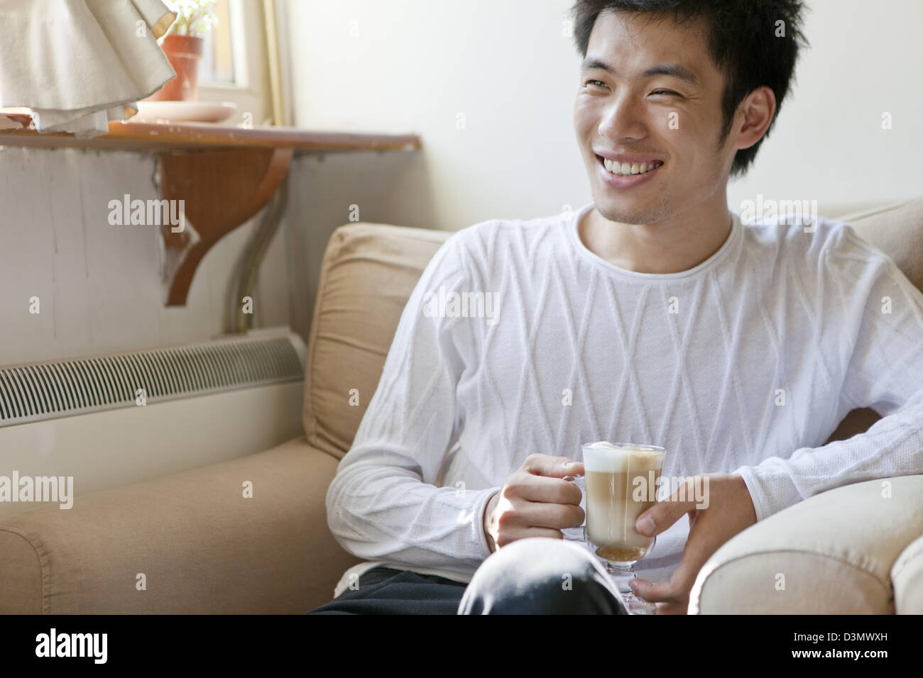 Sorridente giovane uomo cinese in una conversazione di bere il cappuccino Foto Stock